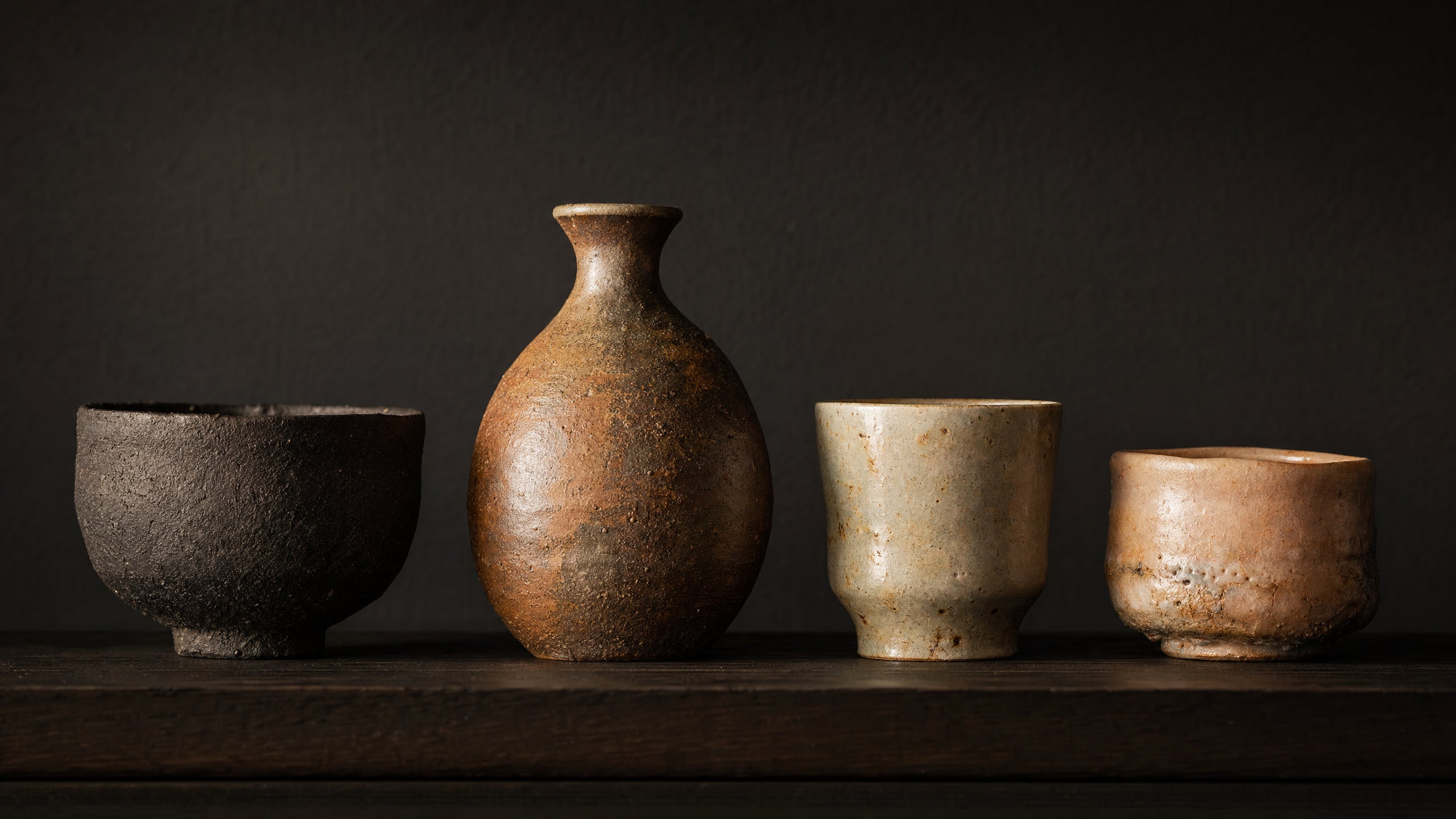A curated collection of Japanese pottery pieces on a dark wooden shelf